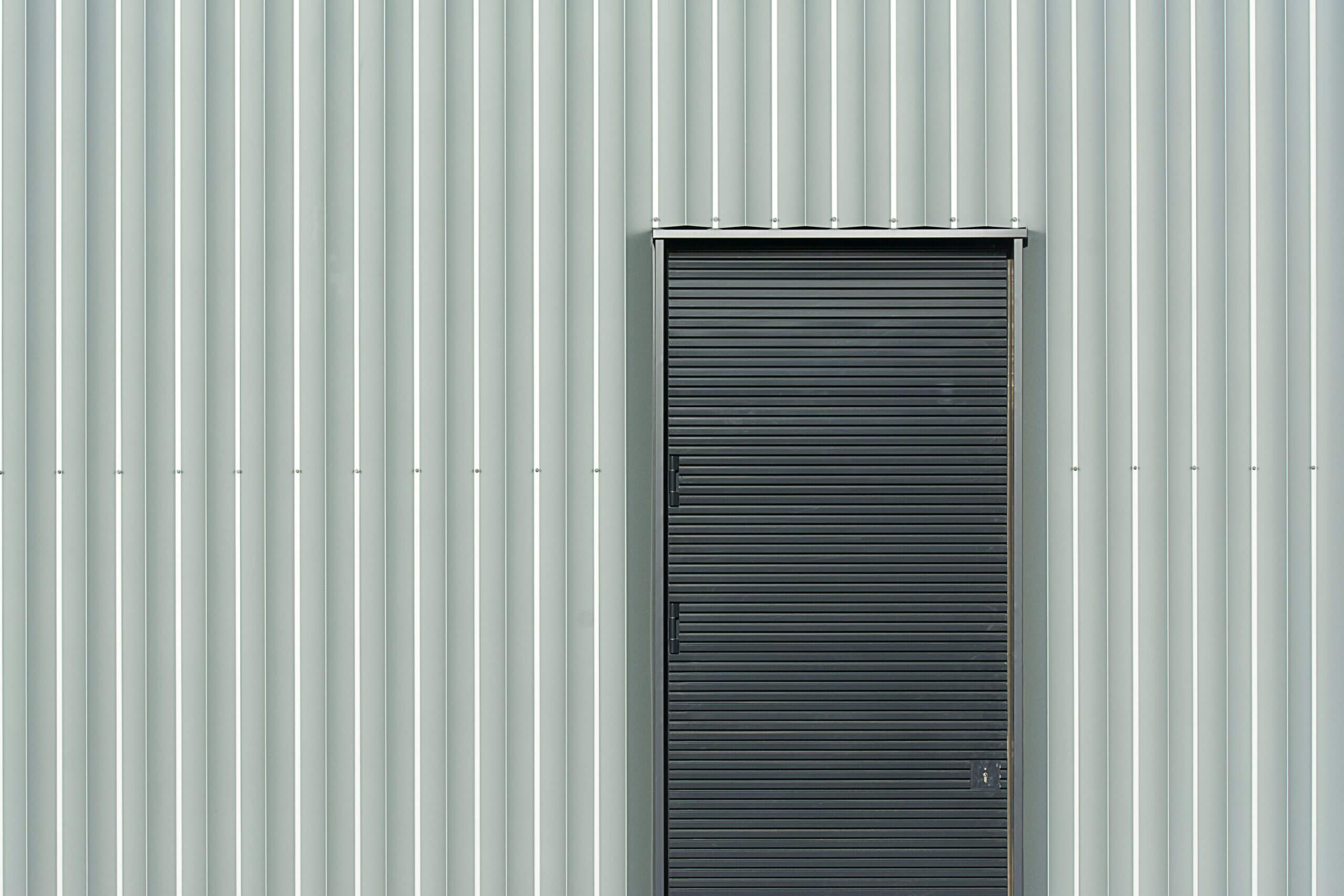 A modern black metal door set against sleek gray aluminum siding, industrial design.