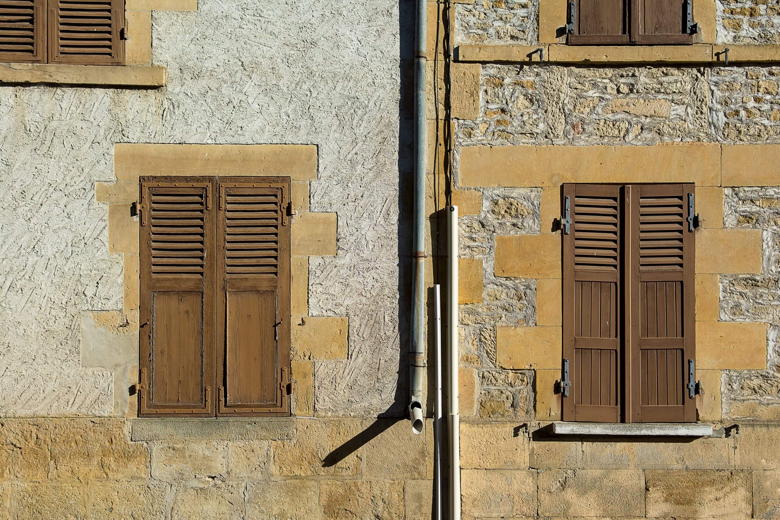 Close-up of a vintage stone facade with wooden shutters, showing rustic charm.