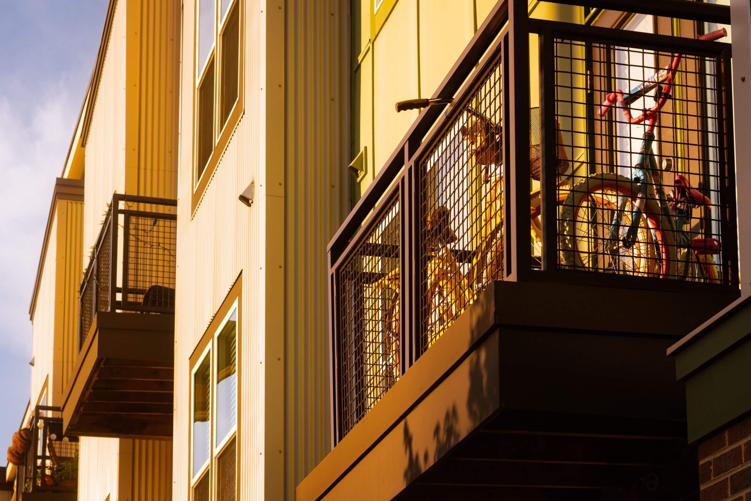 Contemporary residential building featuring metal balconies and parked bicycles, bathed in warm sunlight.