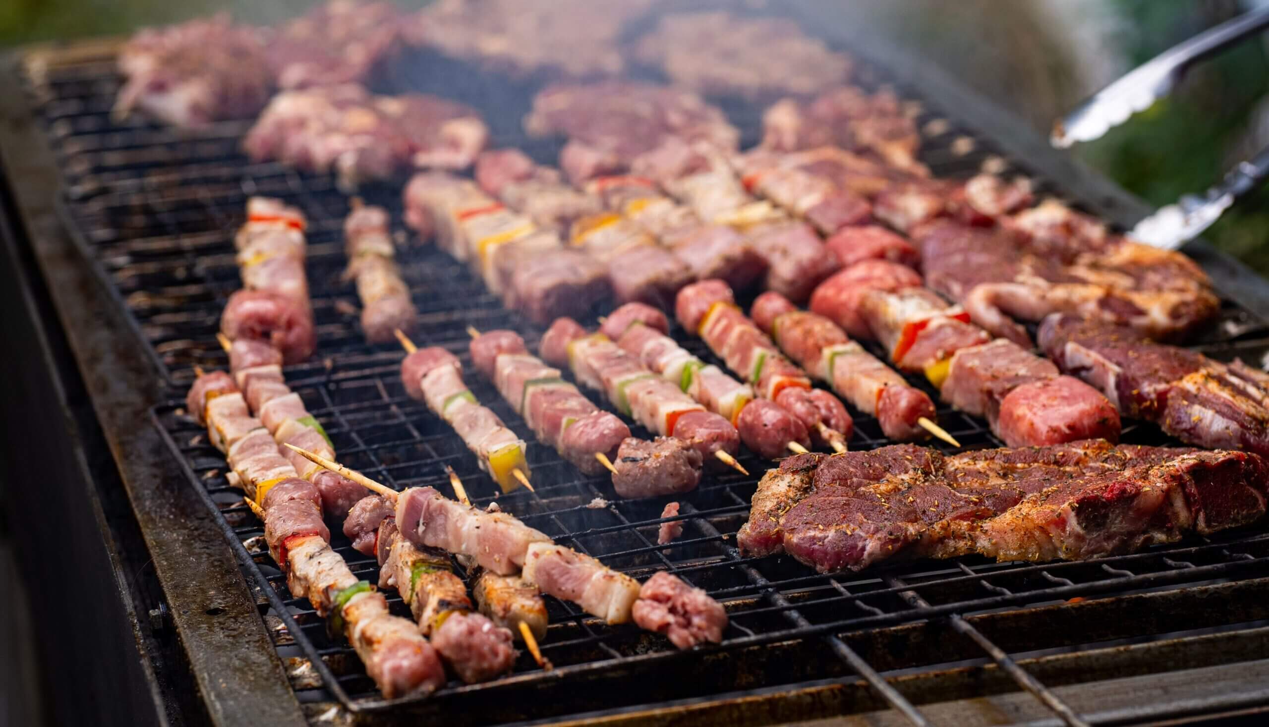 Close-up of various meats and skewers grilling on a barbecue, perfect for outdoor gatherings.