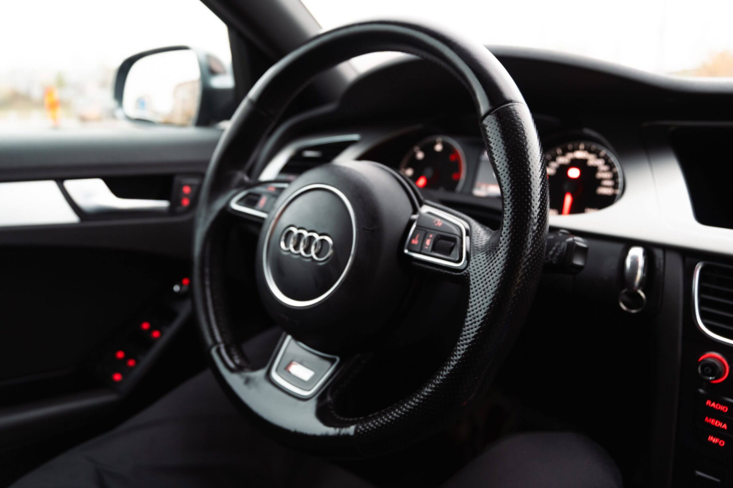 Primo piano del volante di un'auto di lusso con cruscotto e dettagli interni, che enfatizzano eleganza e comfort.