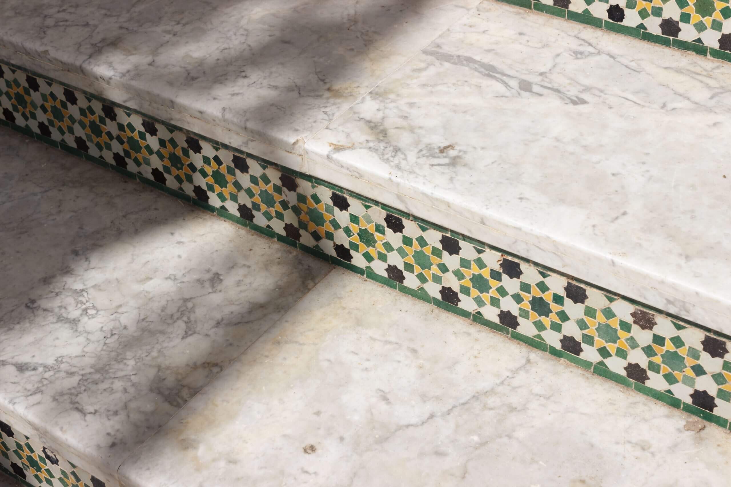 Vista dettagliata di gradini di marmo ornati da intricate tessere di mosaico che proiettano ombre soffuse.